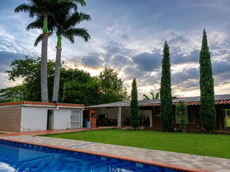 Piscina, palmeras, jard&iacute;n y fachada de Finca Fercho al atardecer